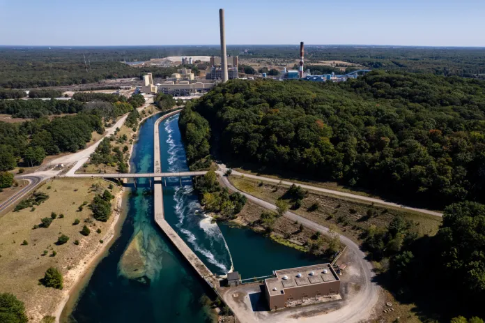 A coal-fired power plant with tall smokestacks stands beyond a line of trees.
