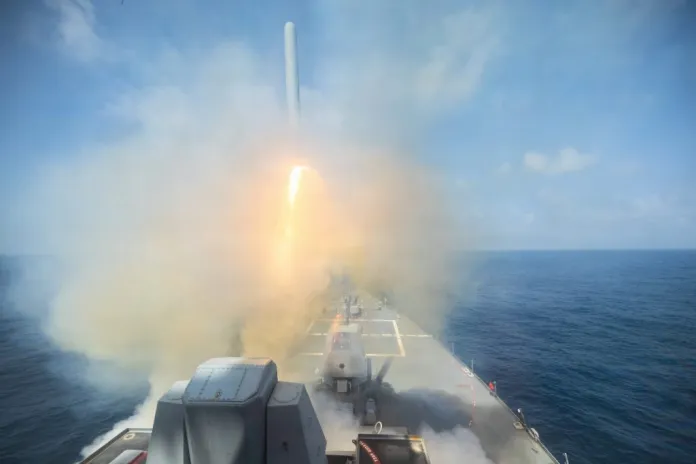 A missile launches from the deck of a naval ship amid smoke over the open ocean.
