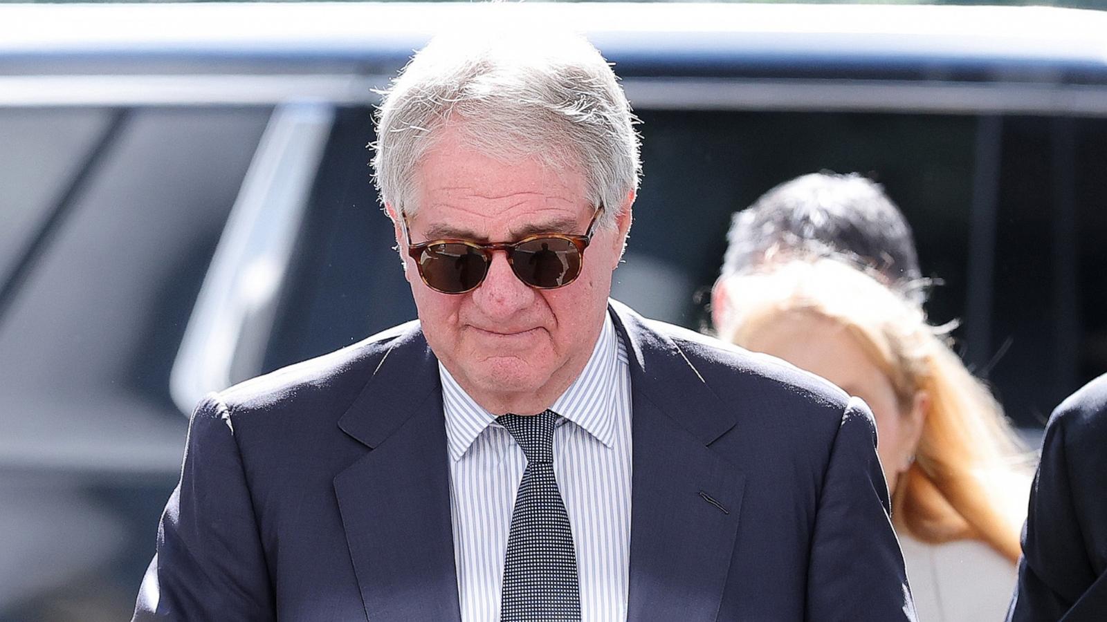 Leon Black in sunglasses and a dark suit, walking outdoors in front of a vehicle.