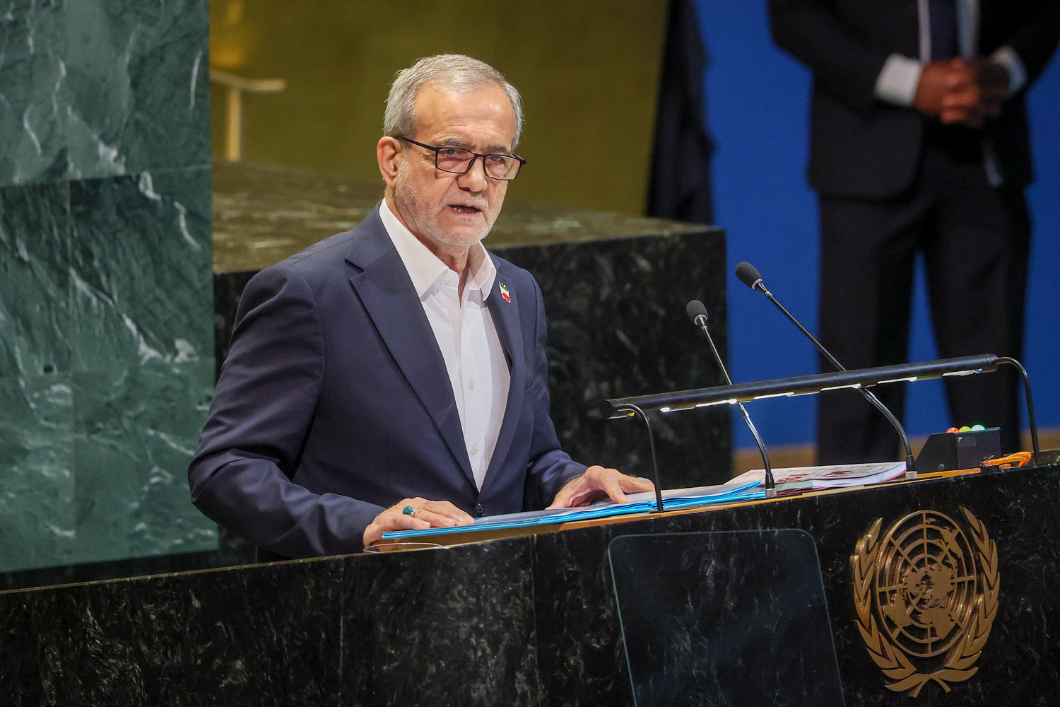 Iranian President Masoud Pezeshkian speaks at the UN General Assembly's green-marble podium, the UN emblem on its front.