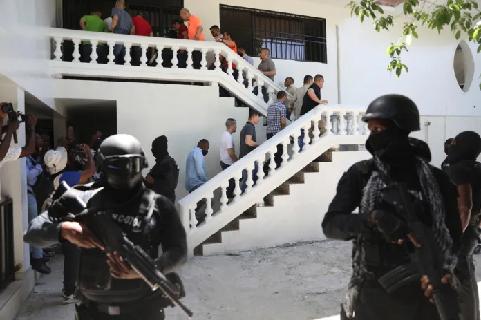 Masked, helmeted guards with rifles escort people down a wide staircase.
