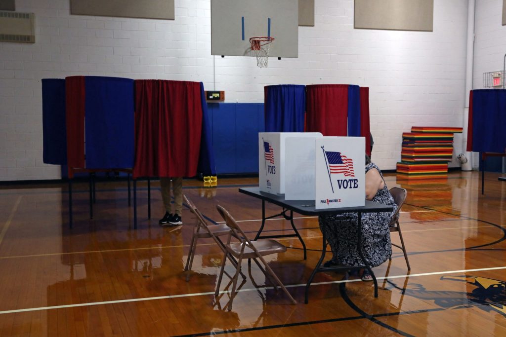 Voters use curtained booths and a tabletop privacy screen inside a gymnasium arranged as a polling place.