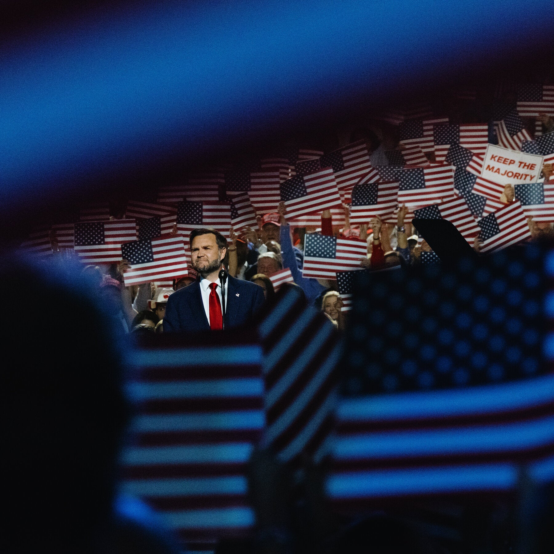 Vance stands at a lectern, framed by a crowd waving small American flags and a Keep the Majority sign.