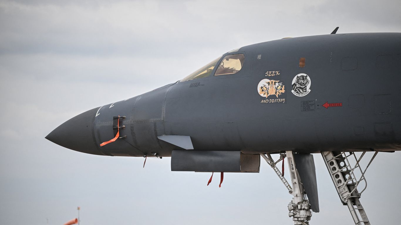 The dark gray nose, cockpit and squadron markings of a B-1 bomber, parked under an overcast sky.
